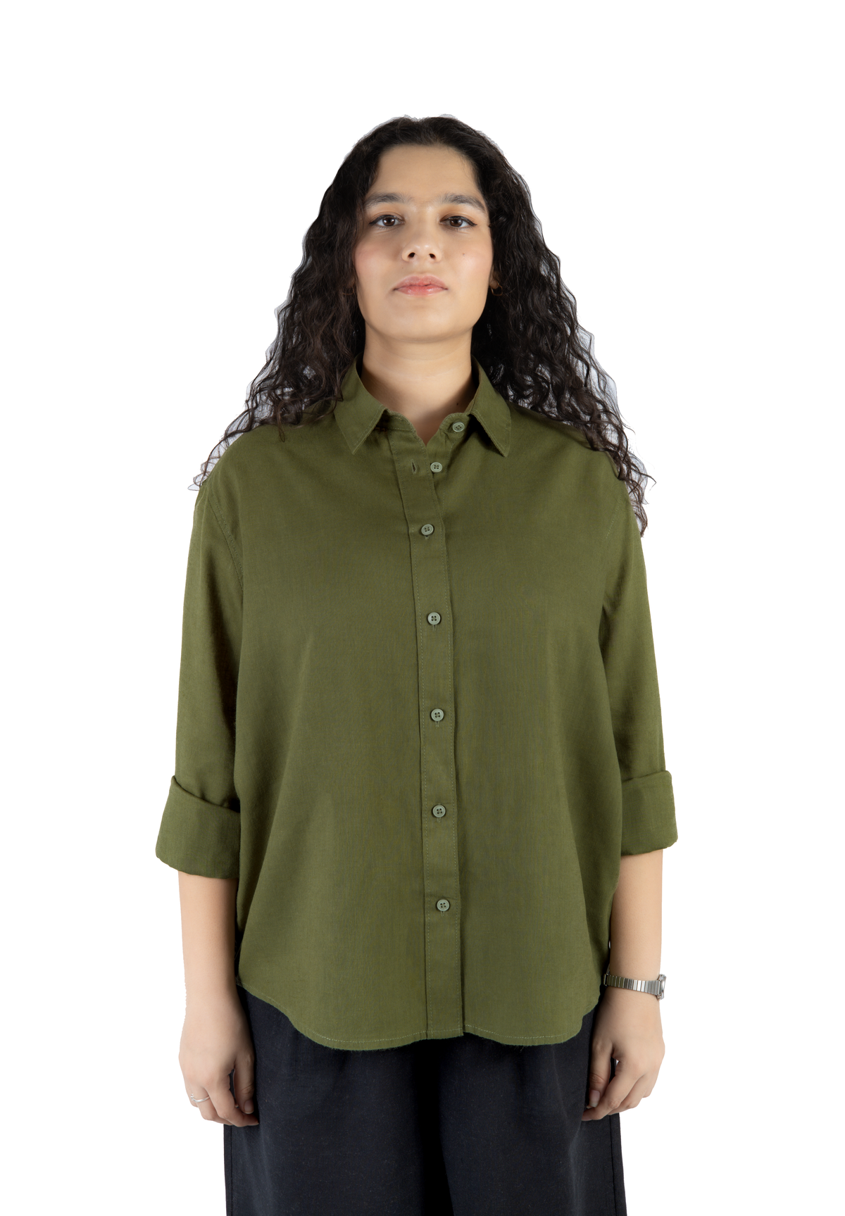 A woman with long, curly dark hair wearing an olive green button-down shirt with rolled-up sleeves and dark pants, standing against a plain white background.