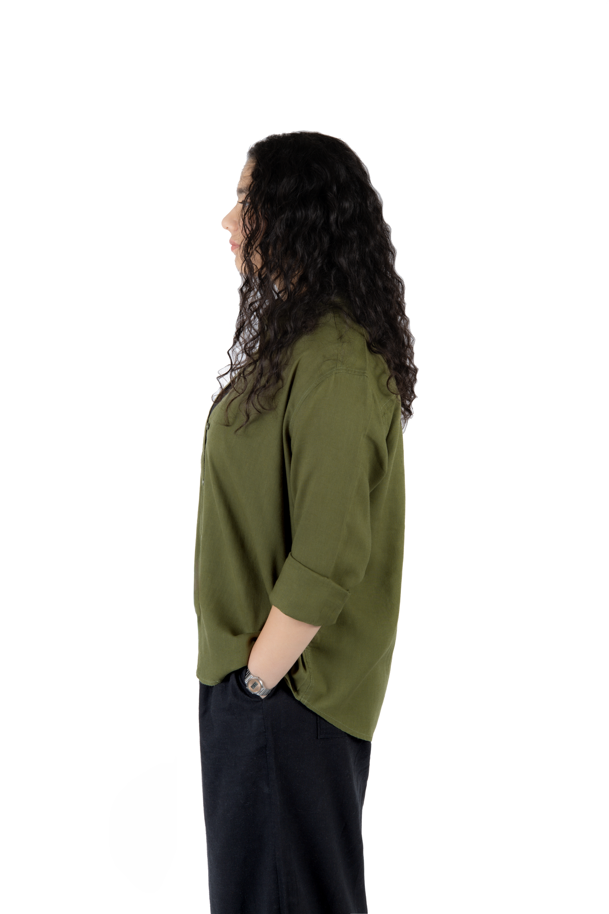 A woman with long, curly dark hair is shown in profile wearing an olive green three-quarter sleeve top and dark pants against a plain white background.