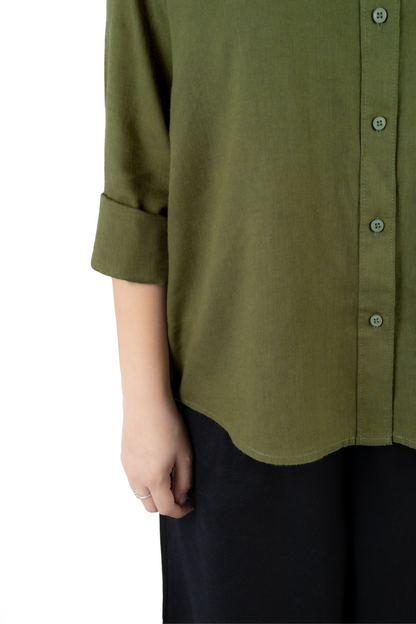 Close-up of a person wearing an olive green button-front shirt with rolled sleeves and dark pants against a plain white background.