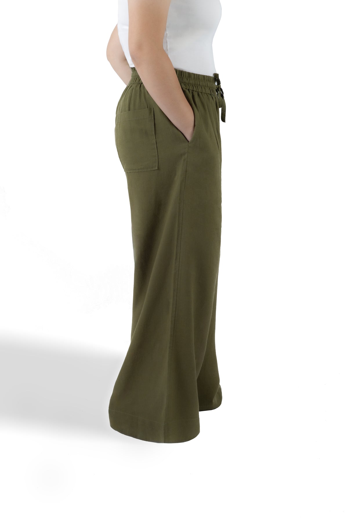 A side-profile view of a model wearing olive green wide-leg pants with a drawstring waistband and side pockets, paired with a white sleeveless top against a white studio background.