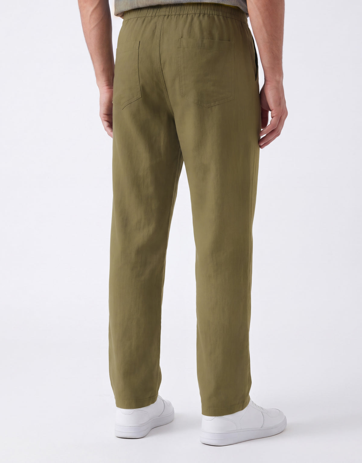 A person shown from the back wearing olive green trousers and white sneakers against a clean white studio background.