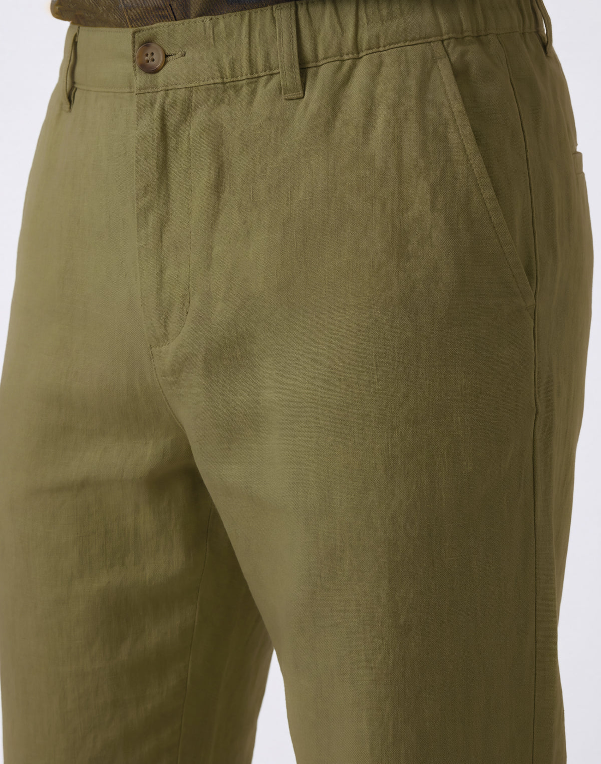 Close-up of olive green trousers on a model, showing the front waistband with belt loops and a brown button, along with the side pocket.