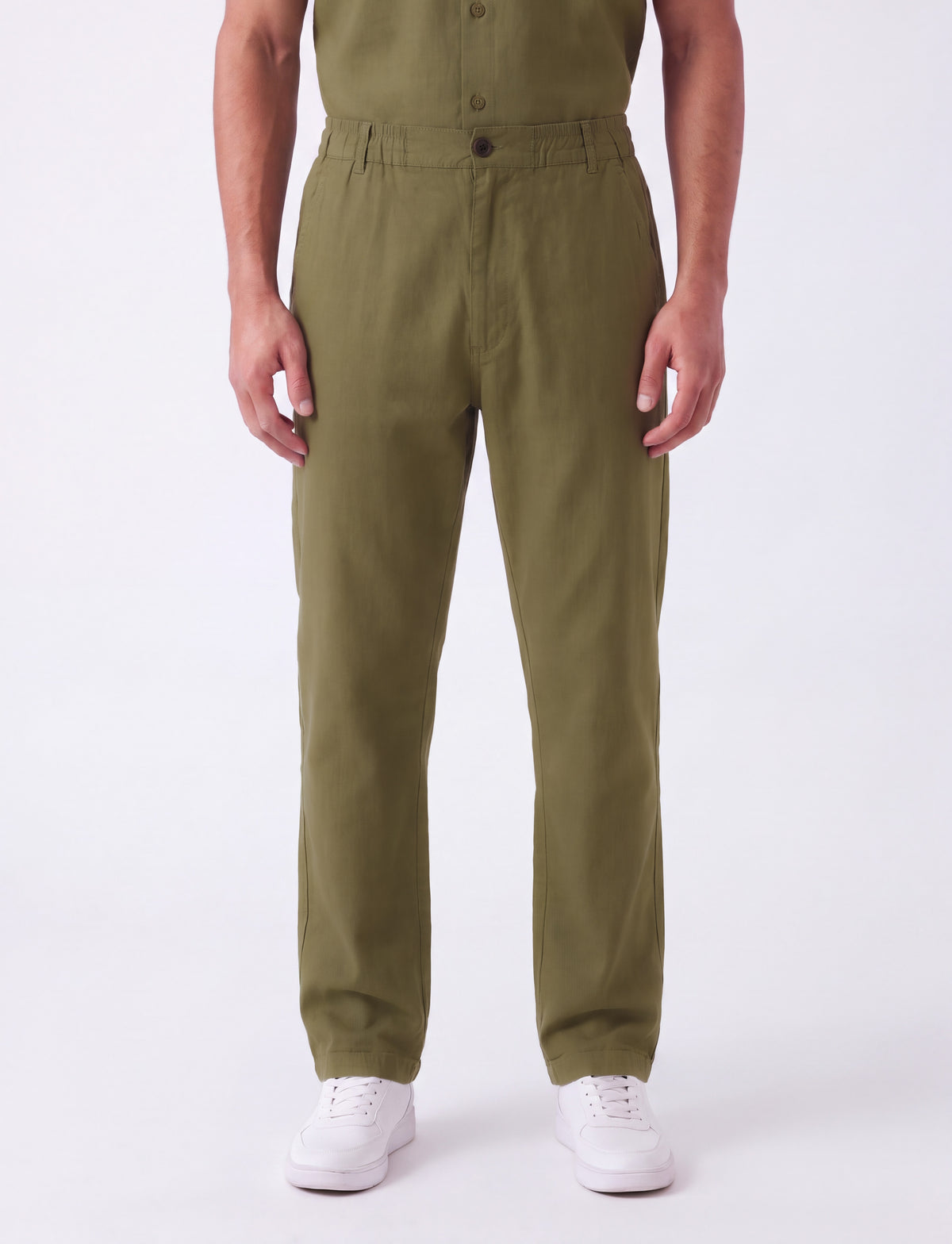 A person wearing olive green straight-leg work pants with white sneakers, shown from the chest down against a plain white studio background.