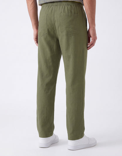 A person shown from the back wearing olive green trousers, a gray top, and white sneakers against a clean white studio background.