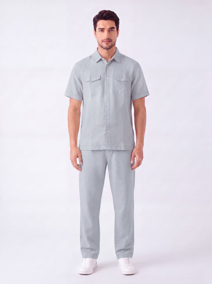 A man modeling a light gray short-sleeve button-up shirt and matching light gray trousers, paired with white sneakers, against a plain white studio background.