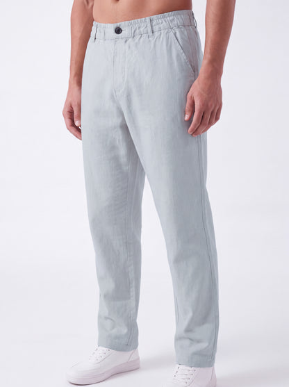 A man wearing light gray linen trousers and white sneakers, shown from the waist down against a plain white studio background.