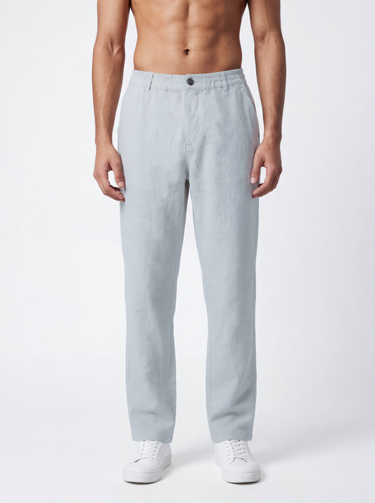 A man wearing light gray relaxed-fit trousers and white sneakers, standing against a plain light gray studio background.