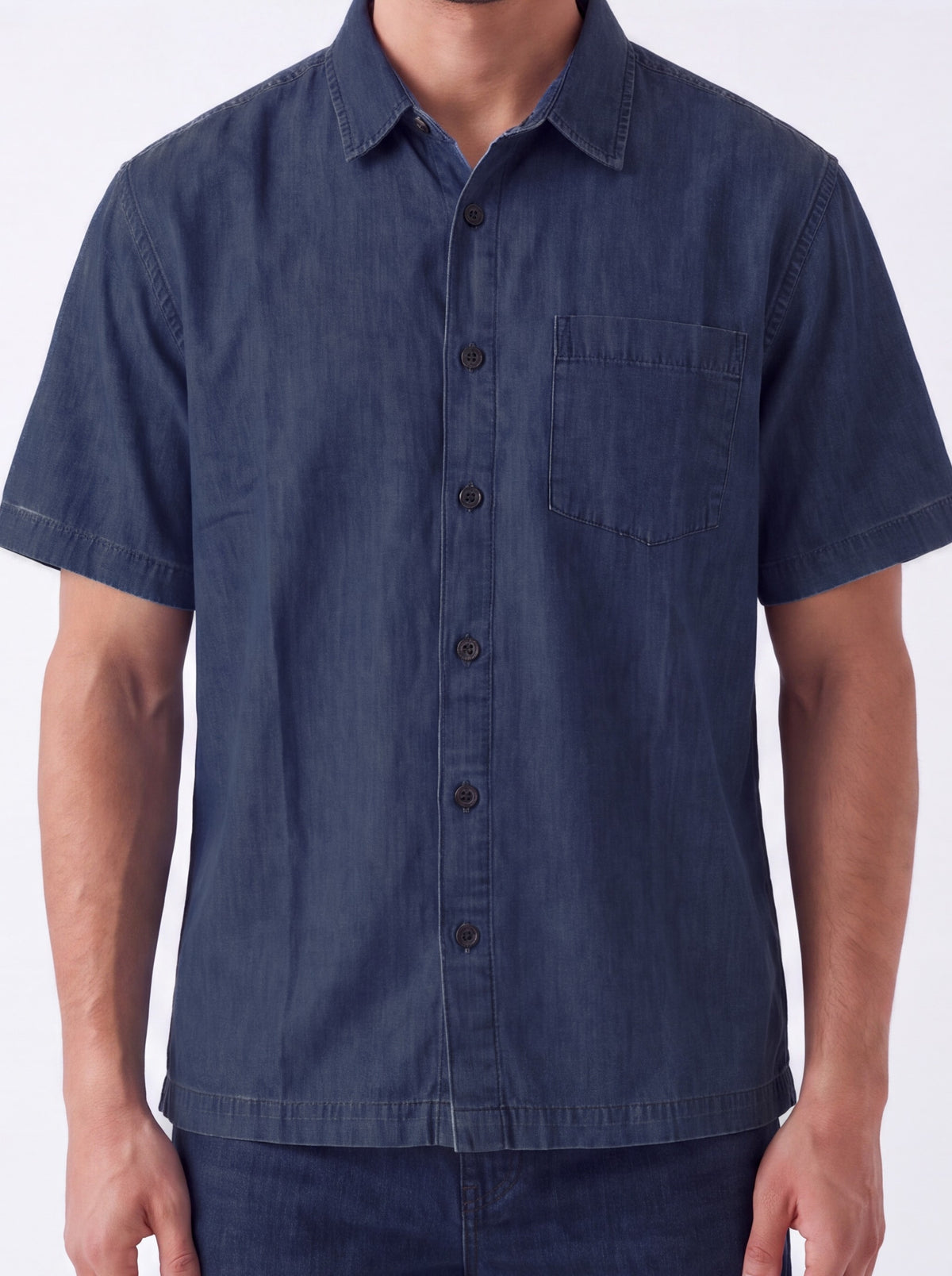 A man wearing a short-sleeve button-up shirt in dark blue chambray fabric, shown from the neck down against a plain white background.