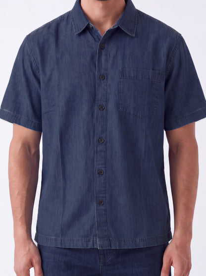 A man wearing a short-sleeve button-up shirt in dark blue chambray fabric, shown from the neck down against a plain white background.