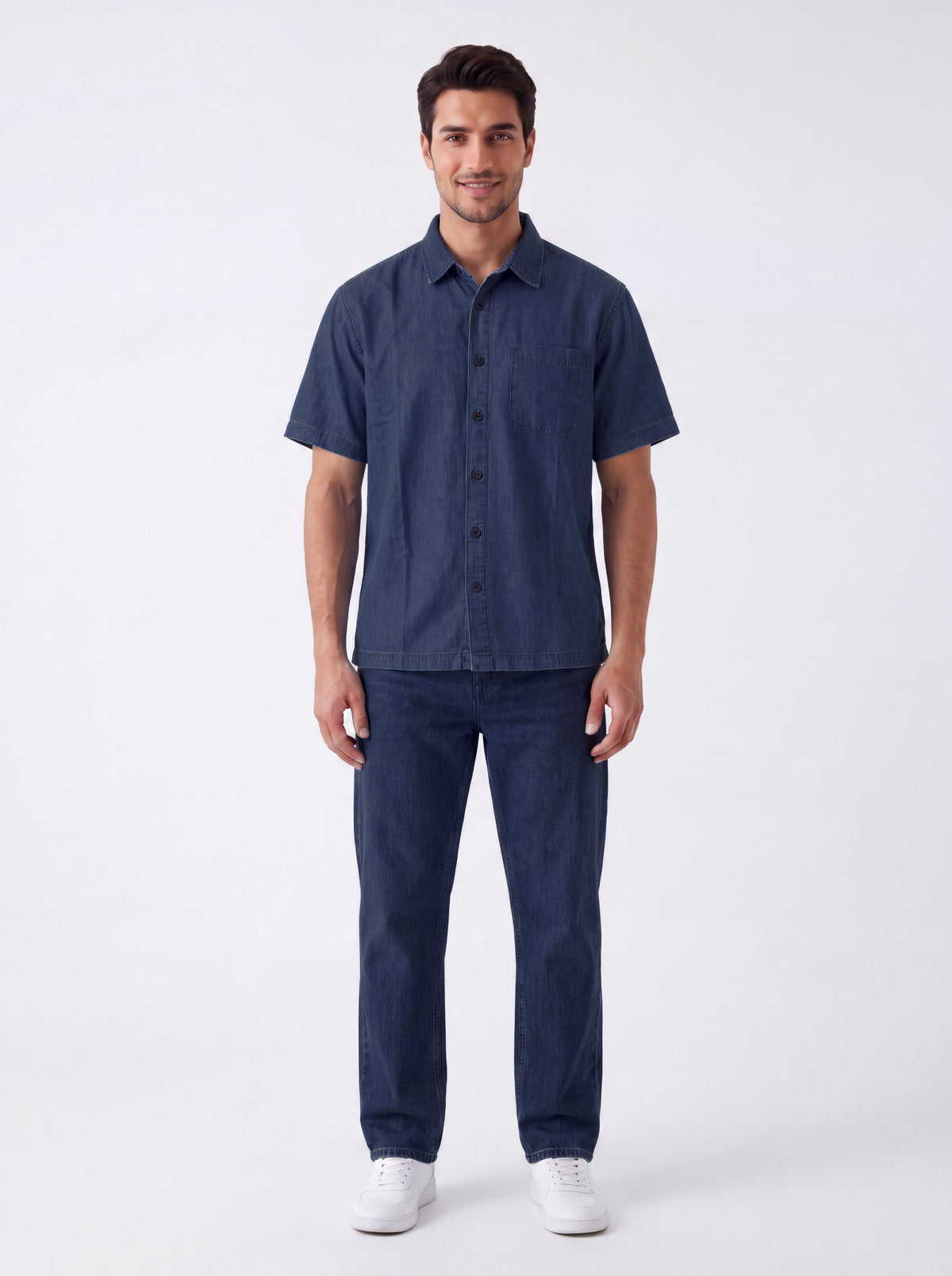 A man modeling a dark blue short-sleeve button-up shirt and matching dark blue jeans against a plain white studio background.