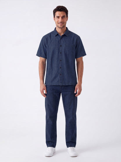 A man modeling a dark blue short-sleeve button-up shirt and matching dark blue jeans against a plain white studio background.