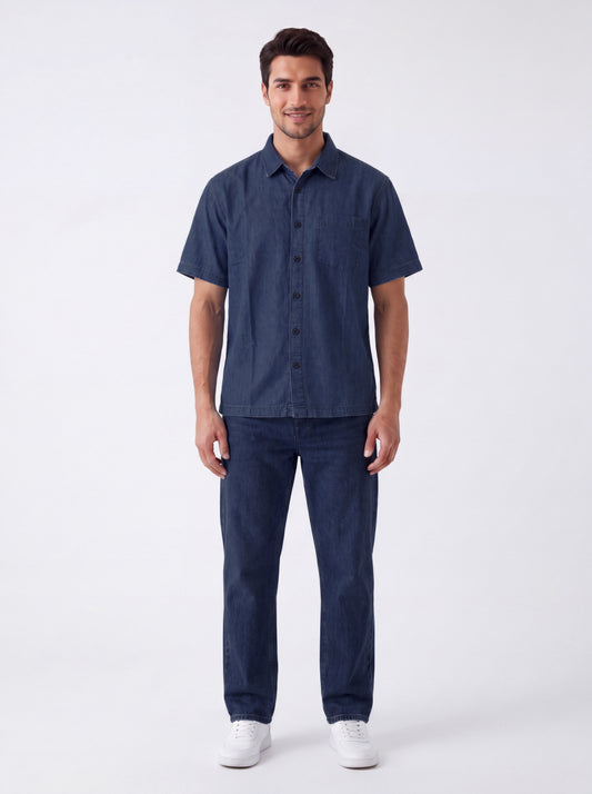 A man modeling a dark blue short-sleeve button-up shirt and matching dark blue jeans against a plain white studio background.