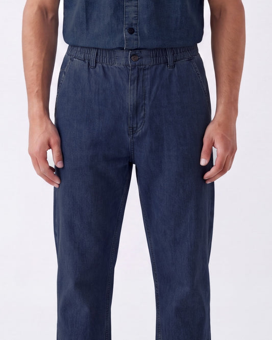 A person wearing dark blue denim work pants with an elastic waistband and button closure, shown from the chest down against a plain white studio background.