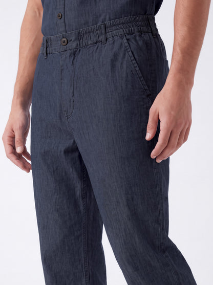 Close-up of a person wearing dark navy blue trousers, showing the waistband, front buttons, side pocket, and hands against a plain light background.