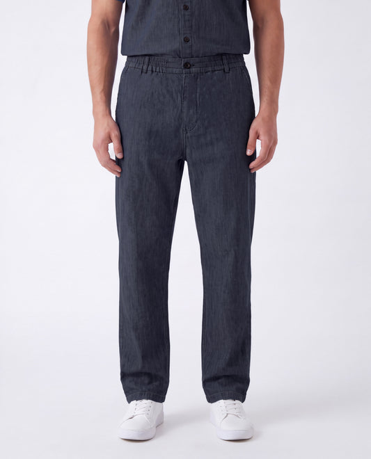 A person wearing dark charcoal gray slim-fit jeans with a button fly and side pockets, paired with a matching dark shirt and white sneakers, photographed against a clean white studio background.