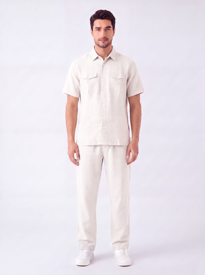 A man modeling a light beige short-sleeve button-up shirt and matching beige trousers against a plain white studio background.