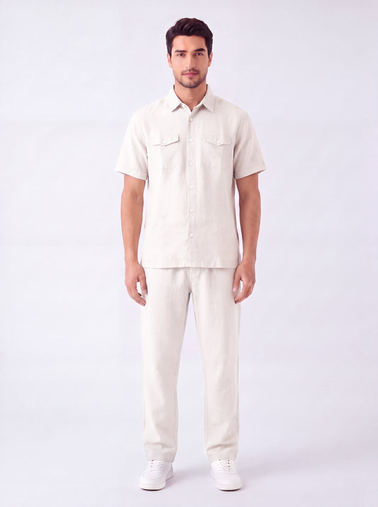 A man modeling a light beige short-sleeve button-up shirt and matching beige trousers against a plain white studio background.