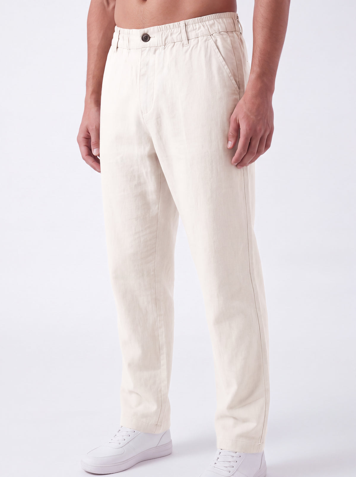 A man wearing off-white linen trousers and white sneakers, shown from the waist down against a clean white studio background.
