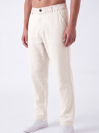 A man wearing off-white linen trousers and white sneakers, shown from the waist down against a clean white studio background.