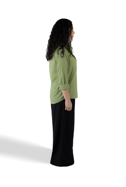 A woman shown from the side profile wearing a sage green three-quarter sleeve top and a long black skirt, standing against a plain white studio background.