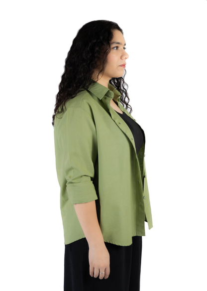 A woman shown in side profile wearing an olive green button-up shirt over a black top and black pants, photographed against a plain white studio background.