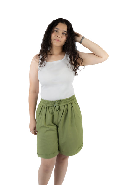 A woman modeling a pair of olive green drawstring shorts and a white tank top against a plain white background.
