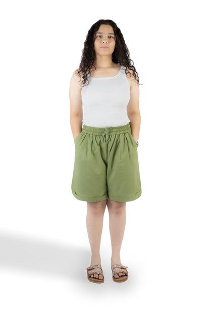A woman modeling a pair of olive green drawstring shorts and a white tank top against a plain white background.