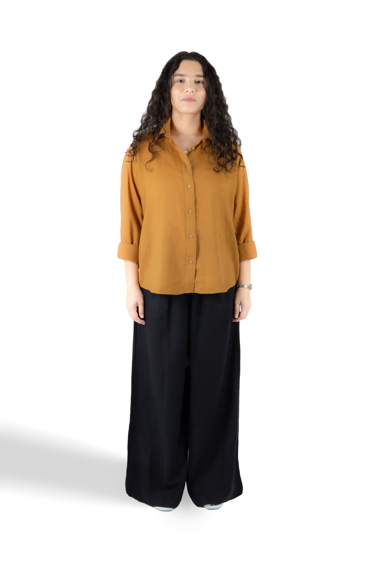A woman modeling a mustard yellow button-up shirt with three-quarter sleeves and black wide-leg pants, standing against a plain white studio background.