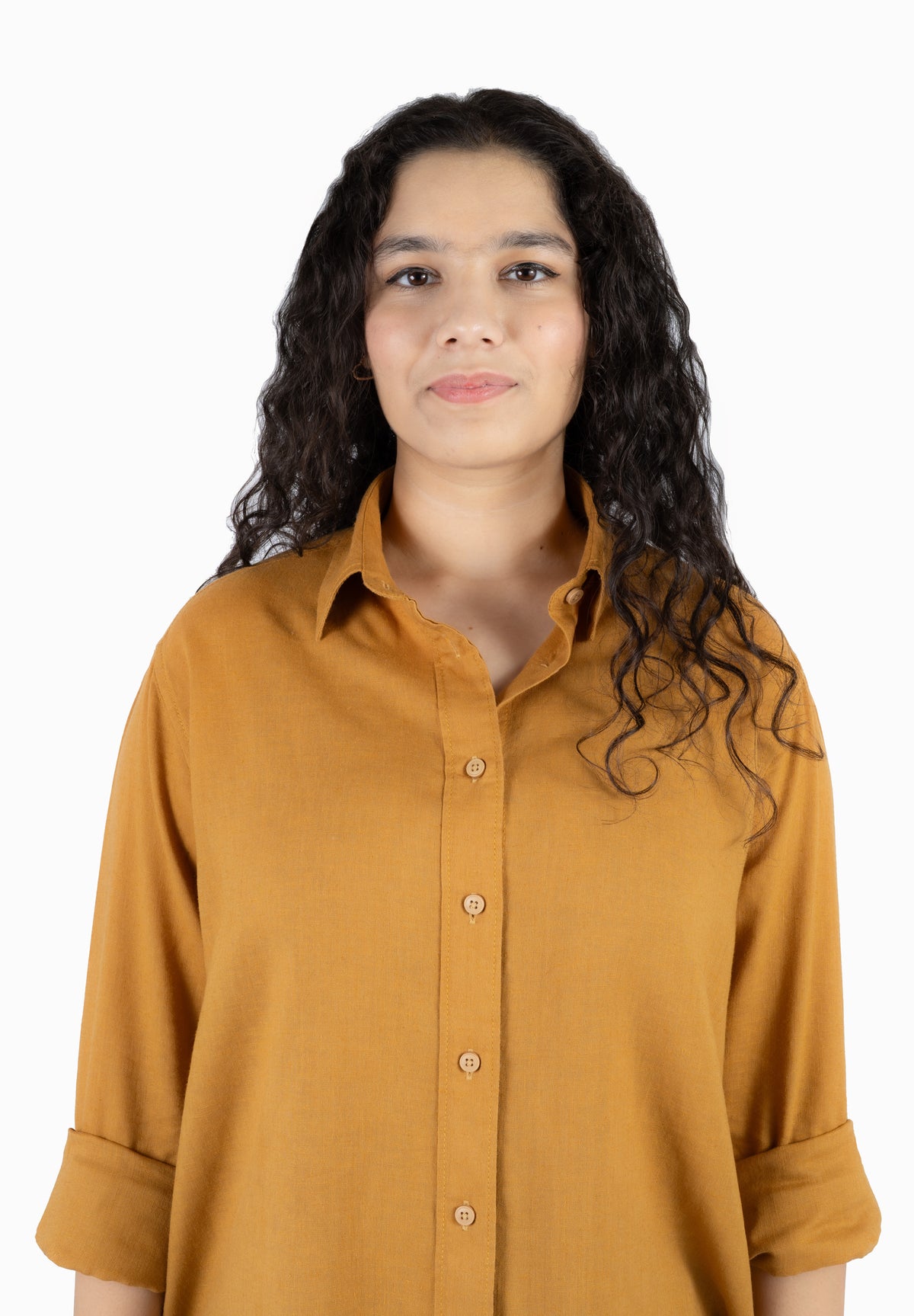 A woman with long, curly dark hair wearing a mustard yellow button-down shirt, photographed against a solid white background.