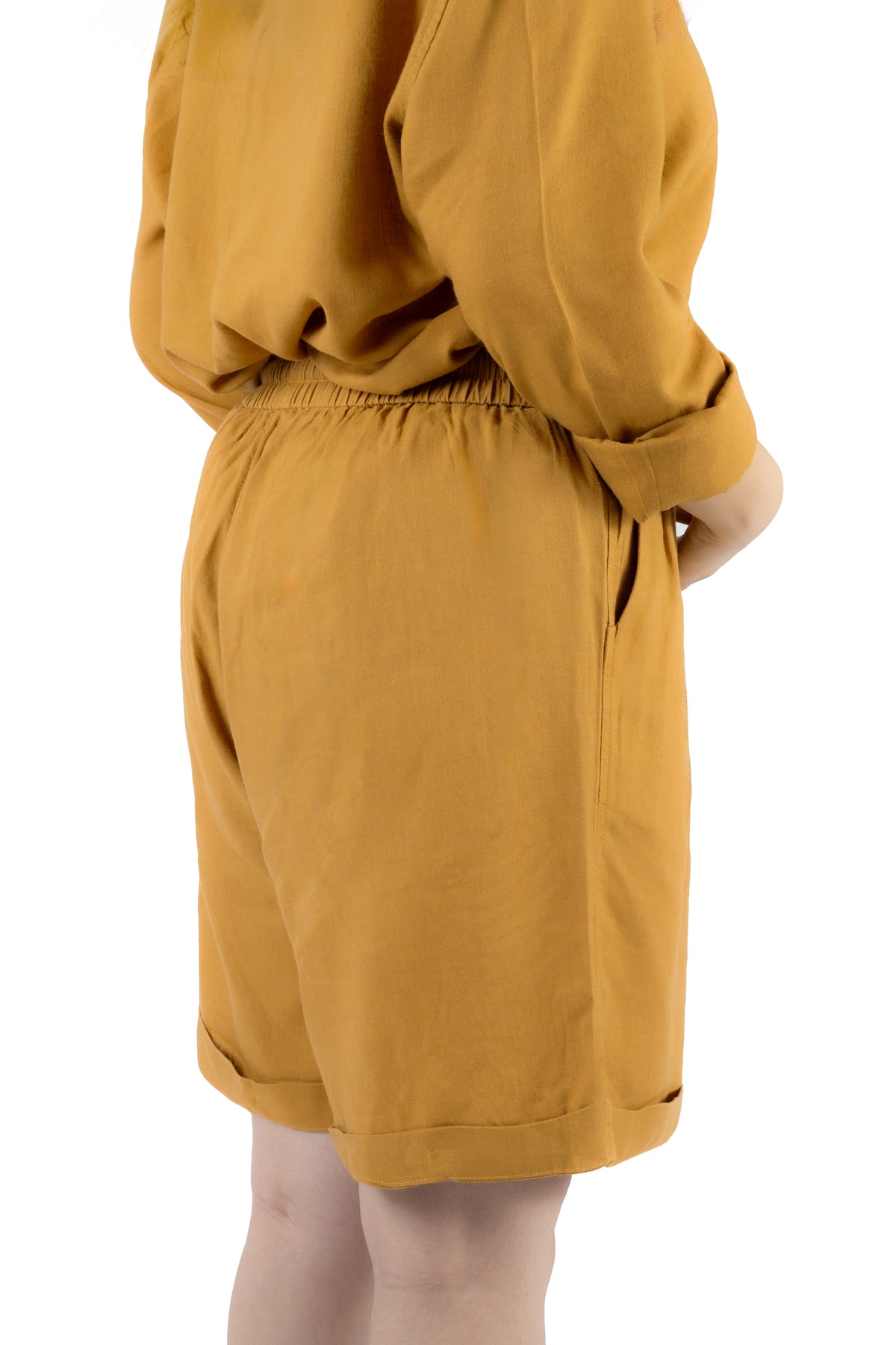 A person wearing a mustard yellow long-sleeve top and matching shorts, shown from the back against a plain white background.