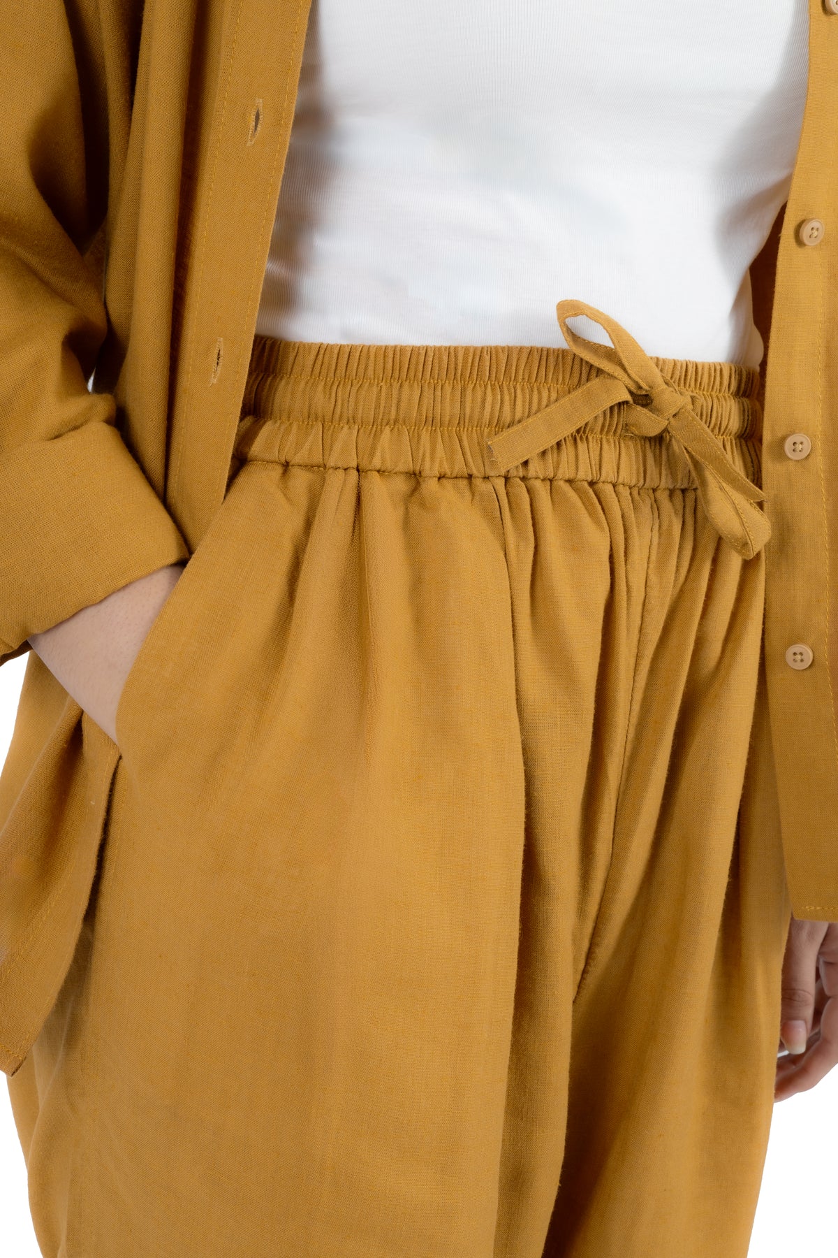 Close-up of a person wearing mustard yellow drawstring trousers with an elastic waistband, styled with a white top and an open mustard cardigan.