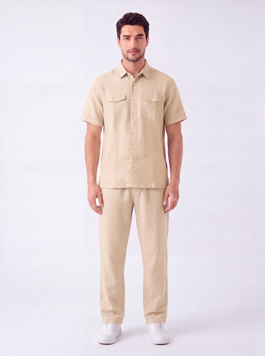 A man modeling a light beige short-sleeve button-up shirt and matching beige trousers against a plain white studio background.