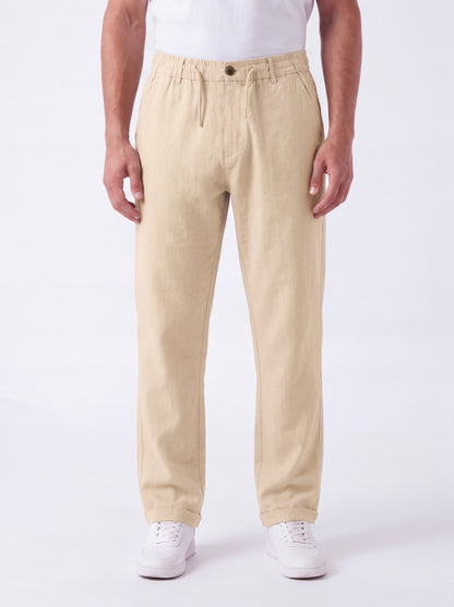 A person wearing beige straight-leg trousers with a drawstring waist, paired with a white t-shirt and white sneakers, standing against a plain white studio background.