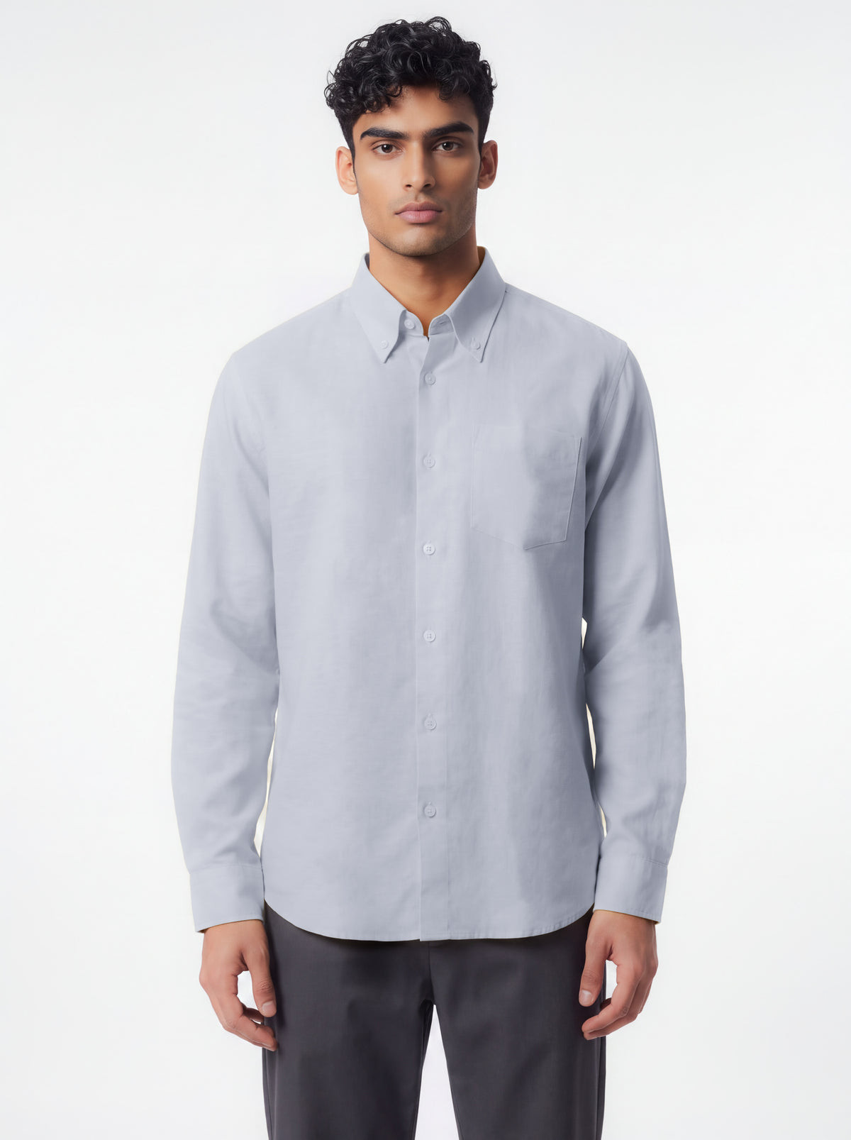 A man wearing a light gray long-sleeve button-down shirt with a pointed collar and dark gray trousers, standing against a plain white studio background.