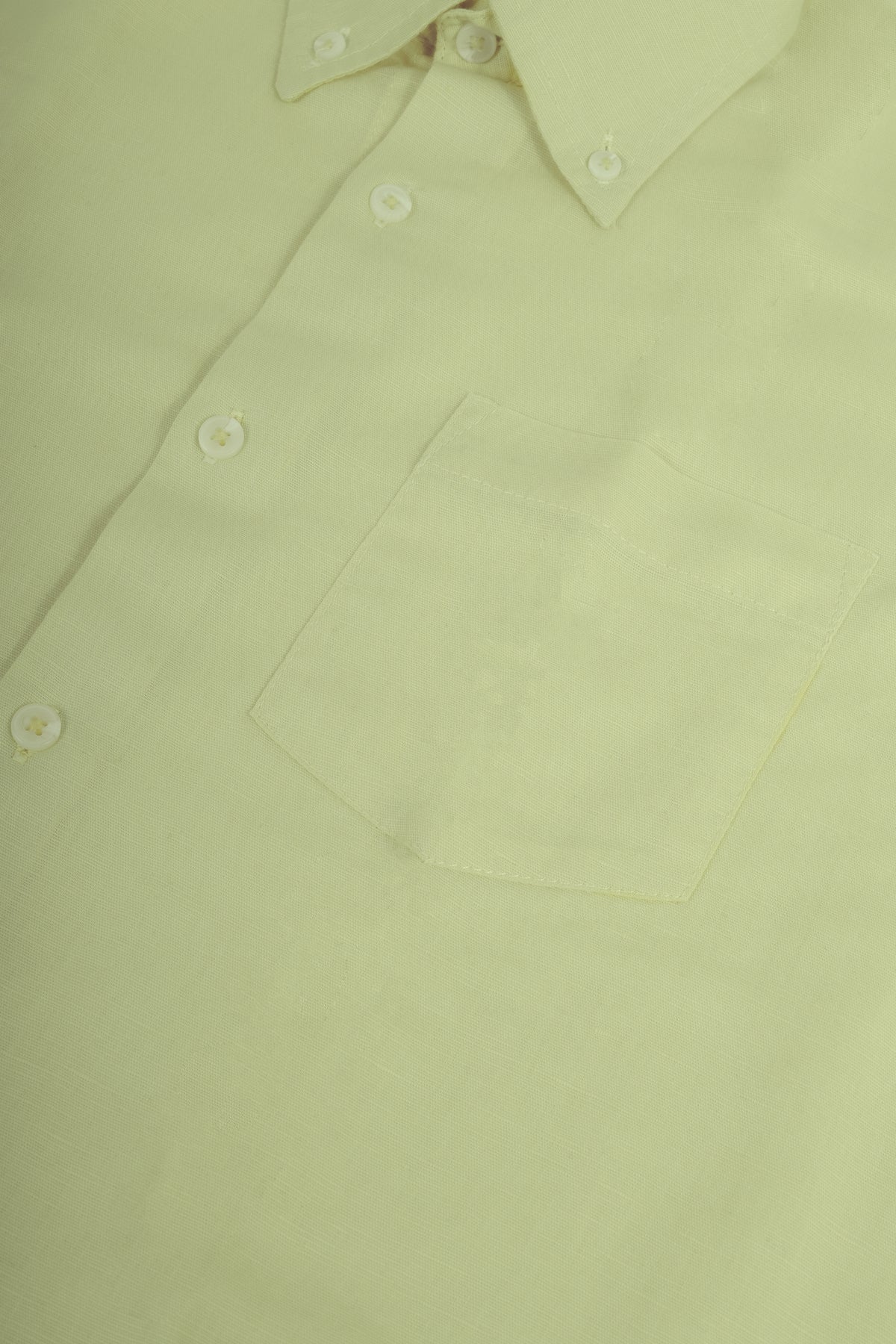 A close-up of a pale yellow-green button-down shirt showing the collar, front buttons, and a chest pocket.