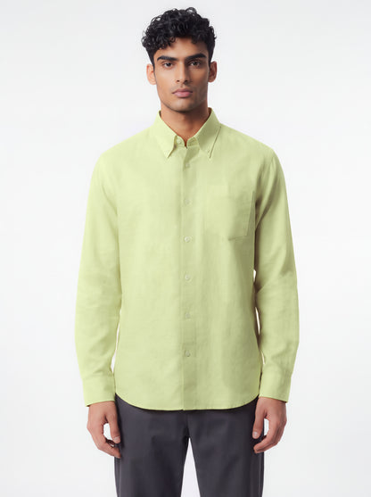 A man wearing a light yellow-green long-sleeve button-down shirt with dark gray trousers, standing against a plain white studio background.