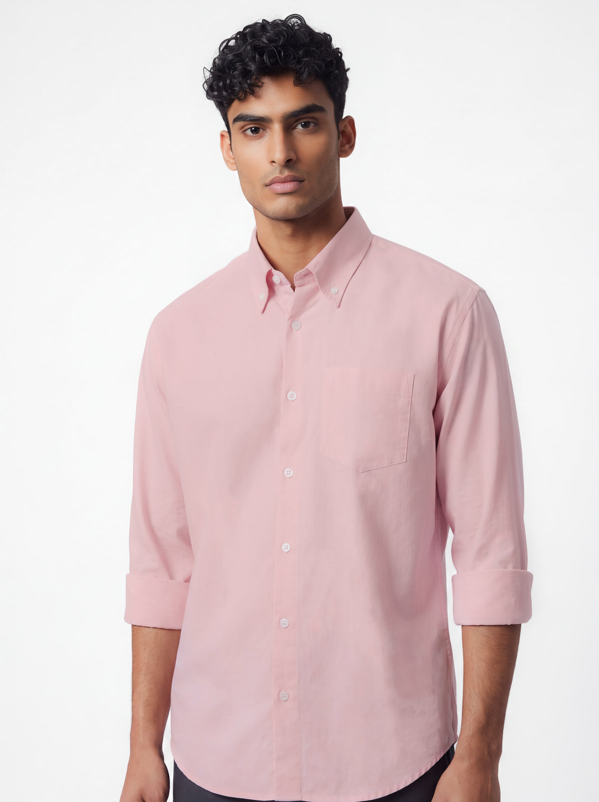 A man wearing a light pink long-sleeve button-down shirt with rolled-up sleeves, shown against a plain white studio background.