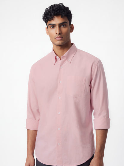 A man wearing a light pink long-sleeve button-down shirt with rolled-up sleeves, shown against a plain white studio background.