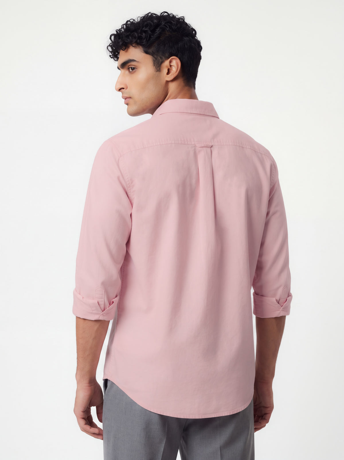 A man wearing a light pink long-sleeve button-down shirt, shown from the back, paired with gray trousers against a plain white studio background.
