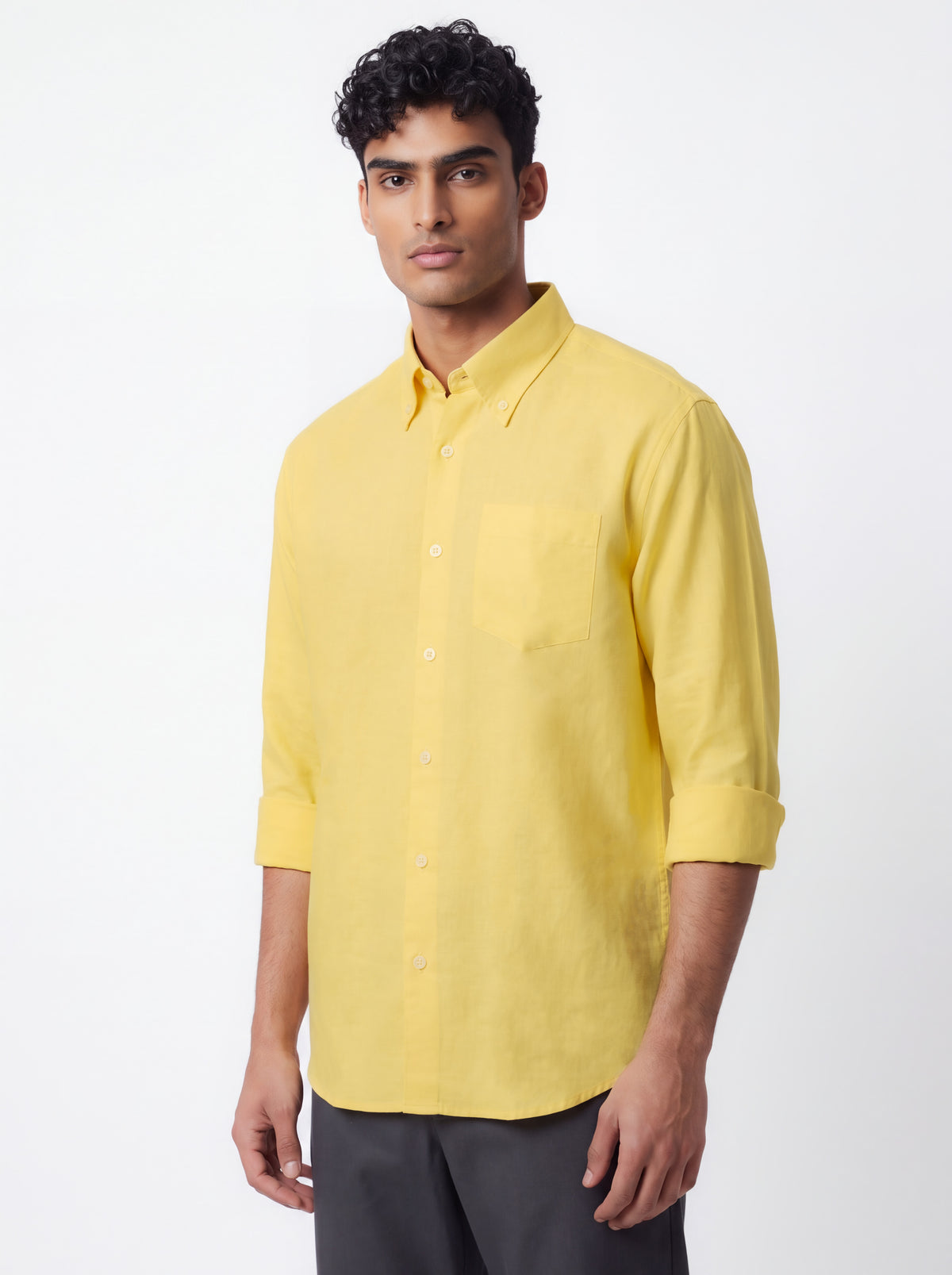 A man wearing a bright yellow, three-quarter sleeve button-down shirt with a chest pocket, paired with dark gray trousers, photographed against a clean white studio background.