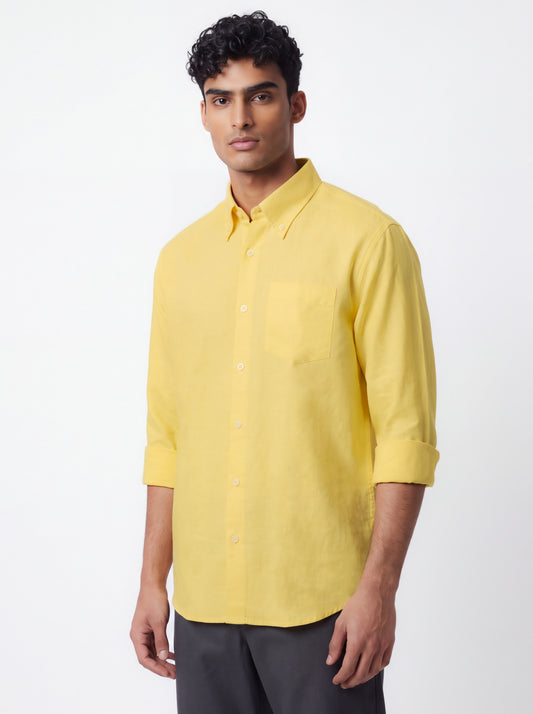 A man wearing a bright yellow, three-quarter sleeve button-down shirt with a chest pocket, paired with dark gray trousers, photographed against a clean white studio background.