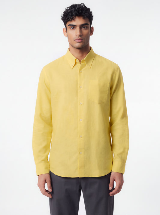 A man wearing a light yellow long-sleeve button-down shirt and dark gray trousers, standing against a plain white studio background.