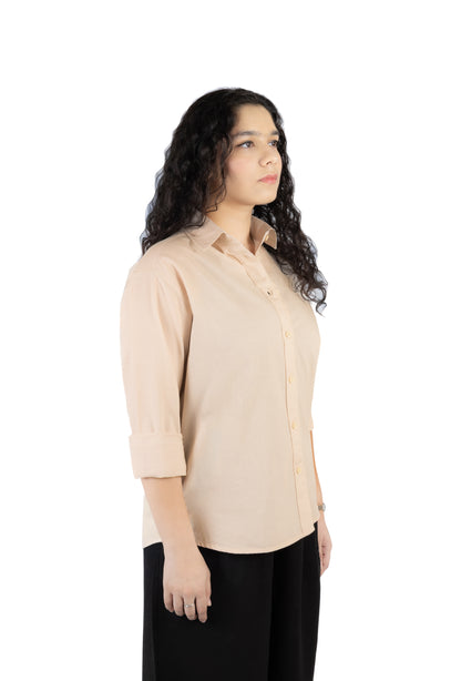 A woman with long, curly dark hair is shown in profile wearing a light beige button-up shirt with rolled-up sleeves and black pants, set against a plain white background.