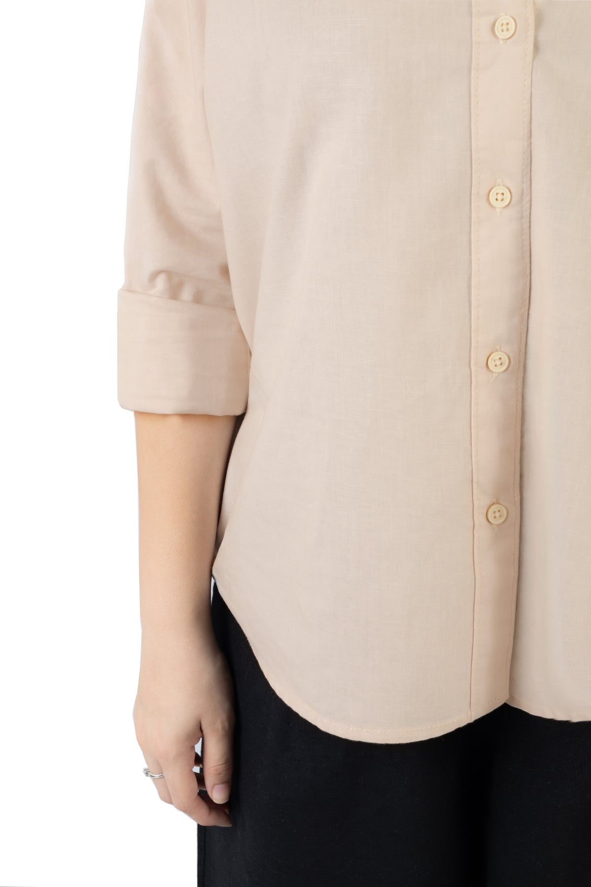 Close-up of a person wearing a light beige linen button-up shirt with rolled sleeves and black pants, against a plain white background.