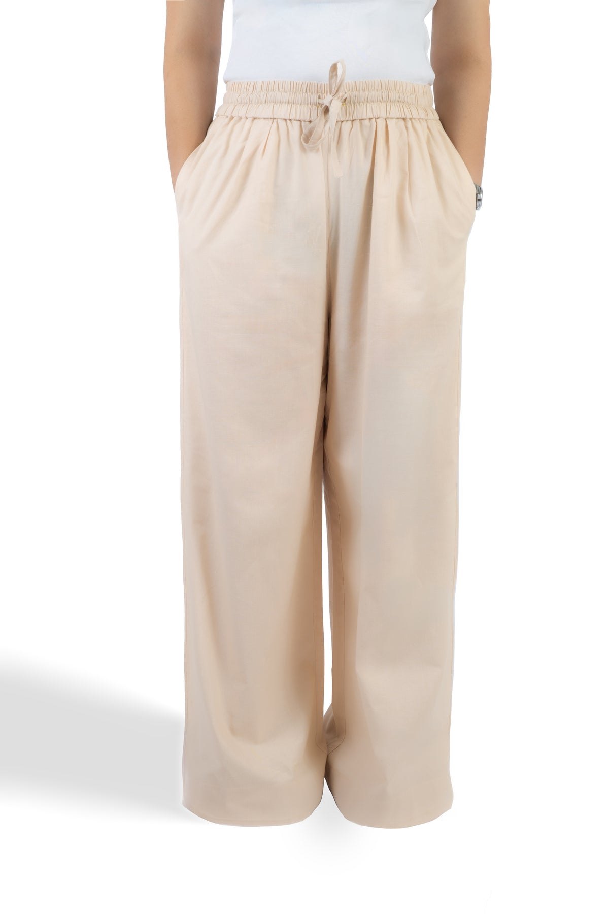 A person wearing loose, wide-leg beige pants with an elastic drawstring waistband, shown from the waist down against a plain white studio background.