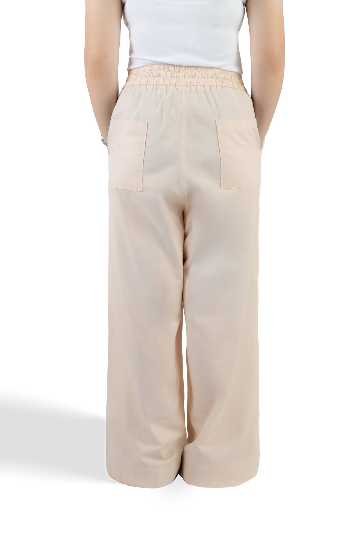 A person shown from the back wearing light beige wide-leg trousers with an elastic waistband and two large patch pockets, paired with a white sleeveless top against a plain white studio background.