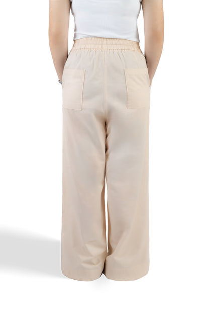 A person shown from the back wearing light beige wide-leg trousers with an elastic waistband and two large patch pockets, paired with a white sleeveless top against a plain white studio background.