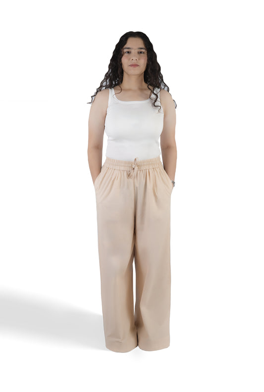 A woman modeling a white sleeveless tank top and beige wide-leg drawstring pants against a plain white studio background.