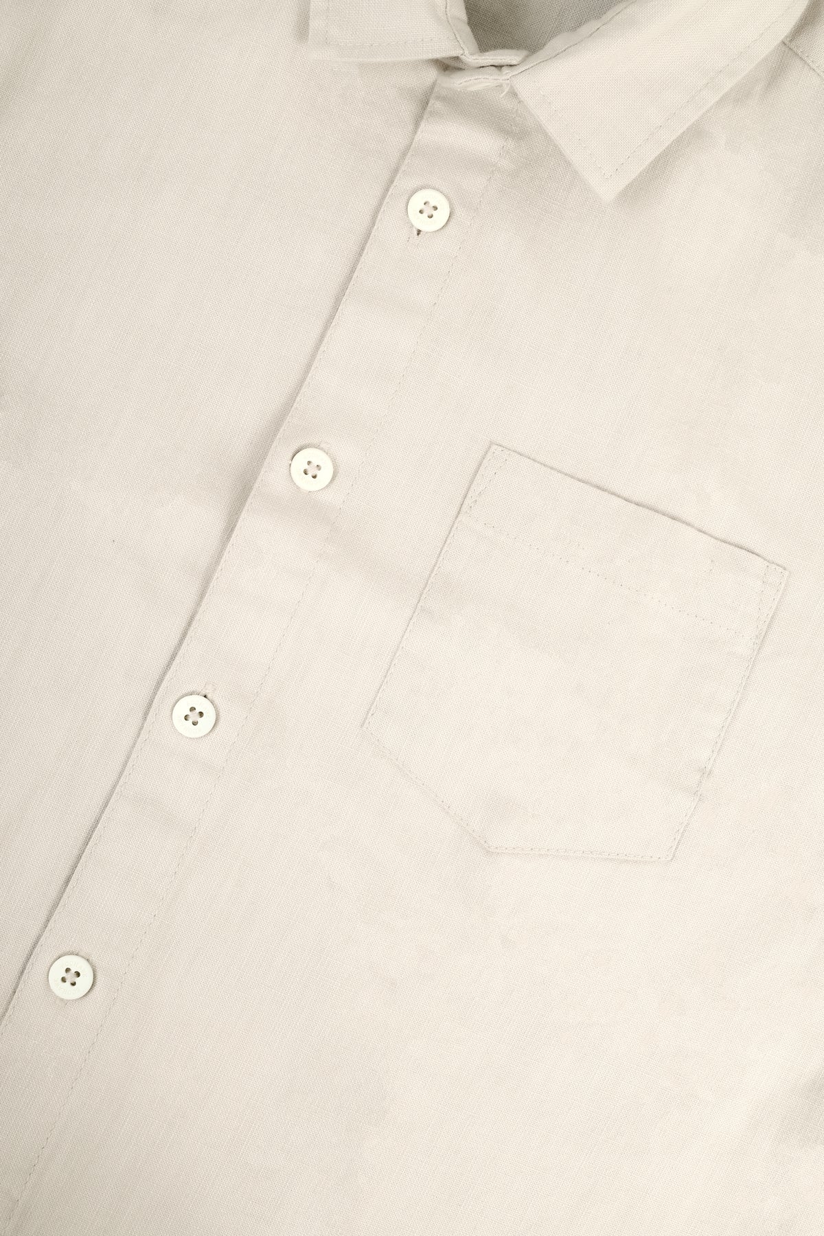 Close-up of a light beige or off-white button-down shirt showing the collar, front buttons, and chest pocket.