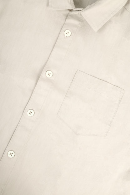 Close-up of a light beige or off-white button-down shirt showing the collar, front buttons, and chest pocket.